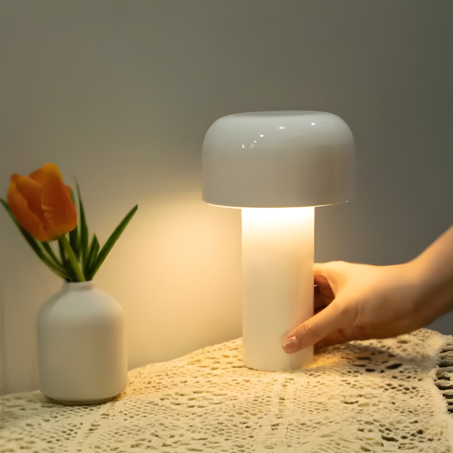 Mushroom-shaped lamp being held by a hand on a textured surface with a vase of flowers in the background.