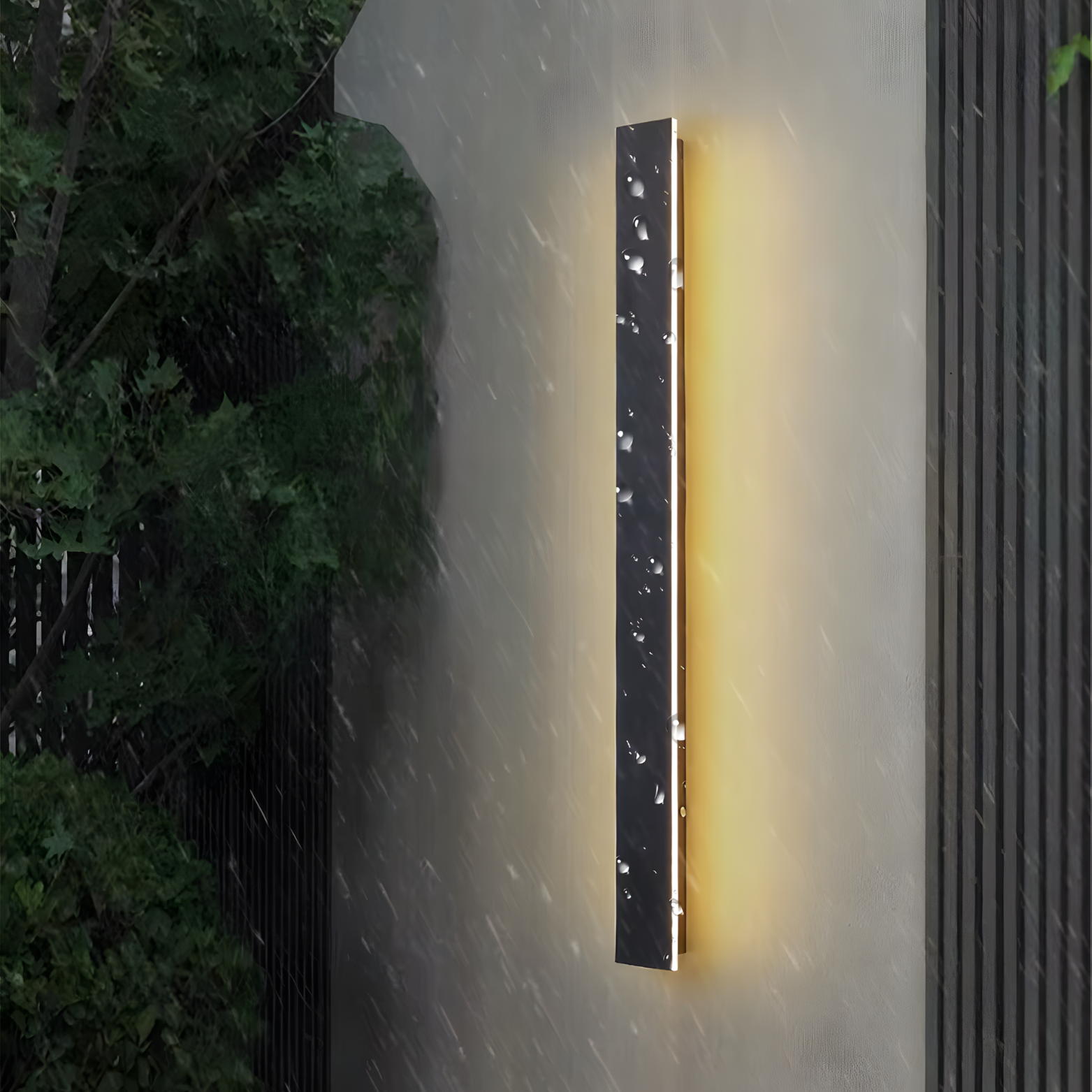 Wall-mounted outdoor light fixture on a gray wall with rain falling