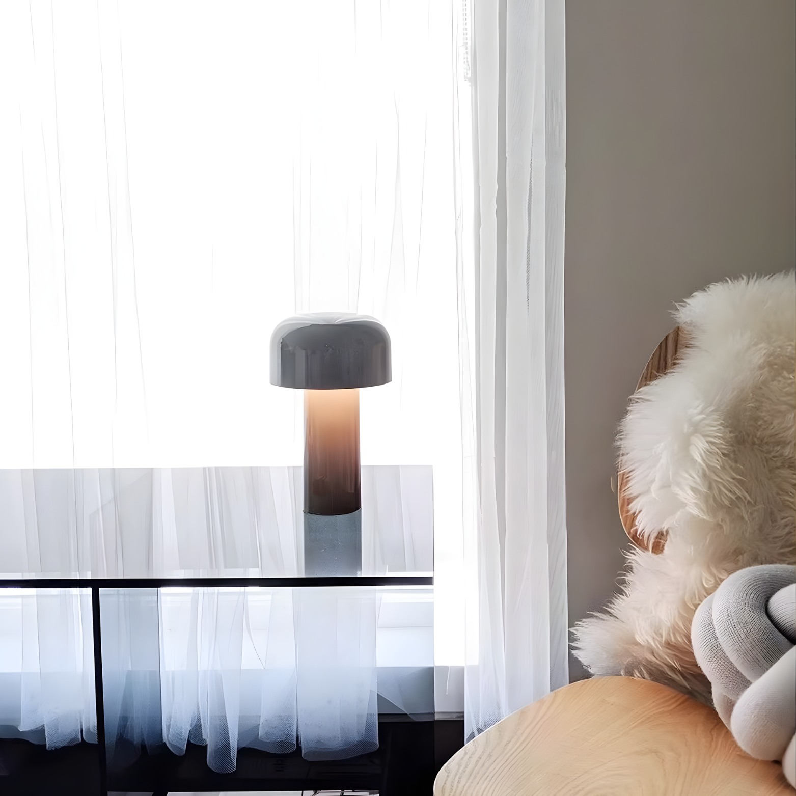 Modern lamp on a table with a soft light, next to a plush toy and sheer curtains.