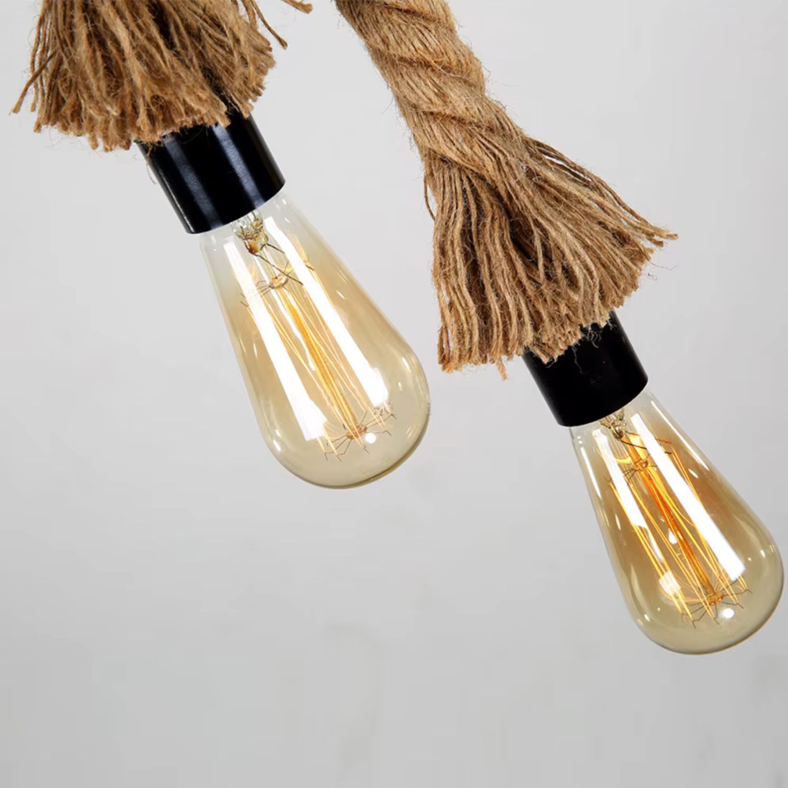 Two vintage-style light bulbs hanging by braided twine against a plain background