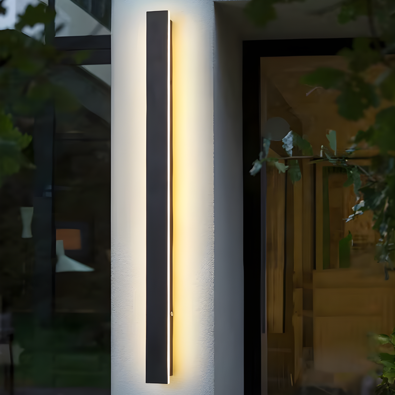 Modern outdoor wall light fixture on a building exterior with plants in the background.