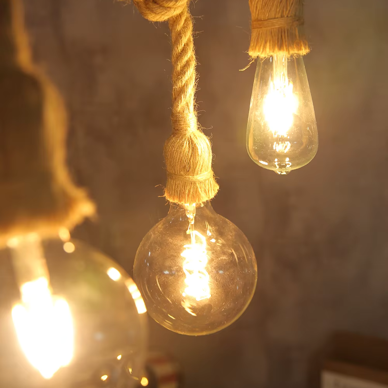 Three vintage-style light bulbs hanging by ropes against a textured wall.