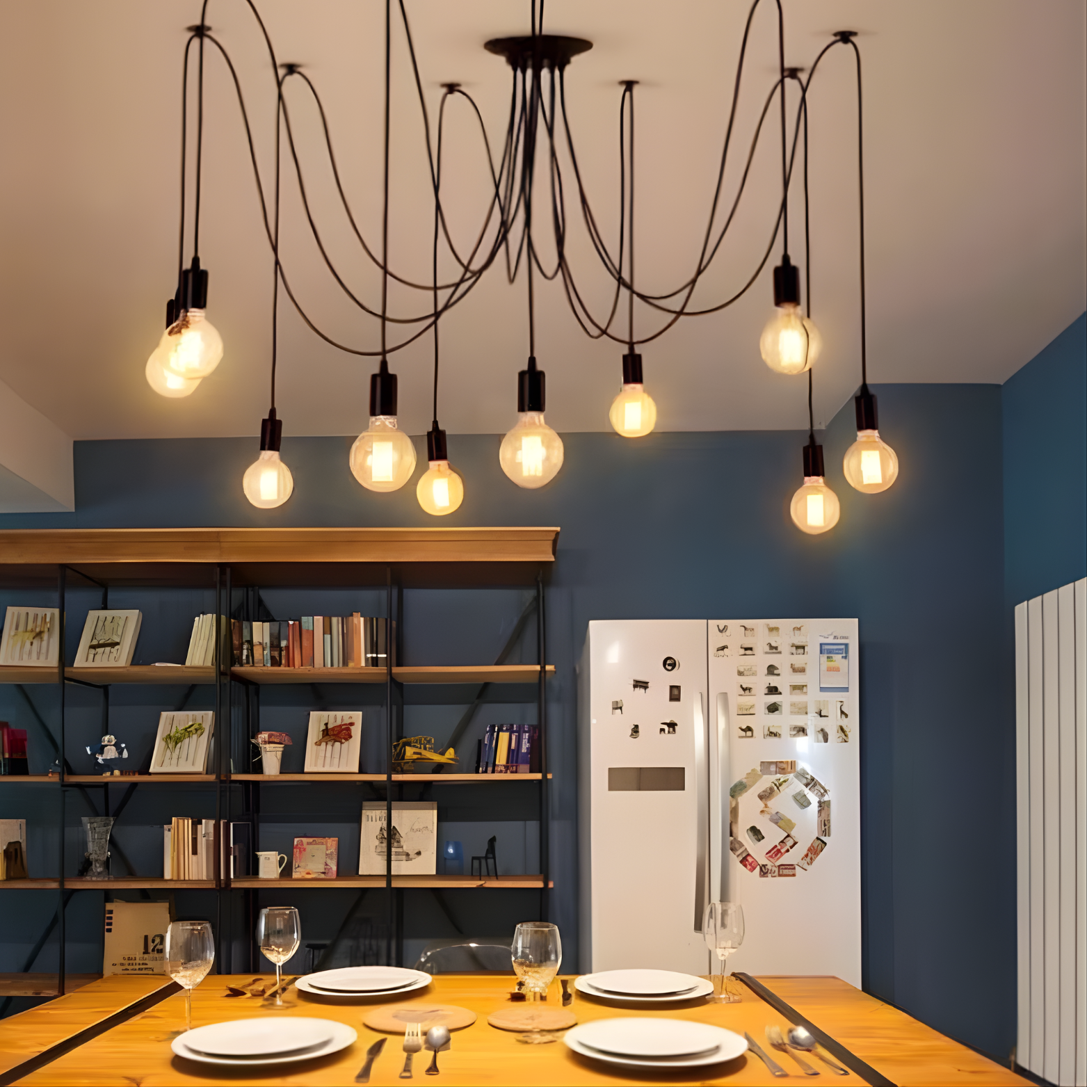 Modern kitchen with hanging light fixtures, a refrigerator, and a dining table.