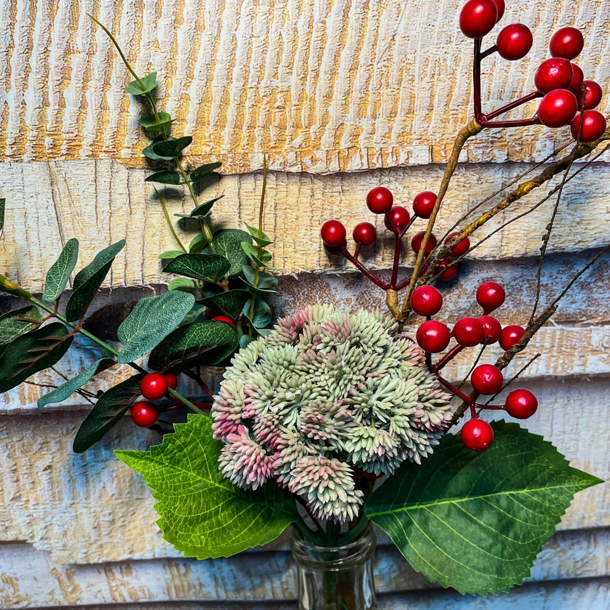 a vase filled with red berries and green leaves