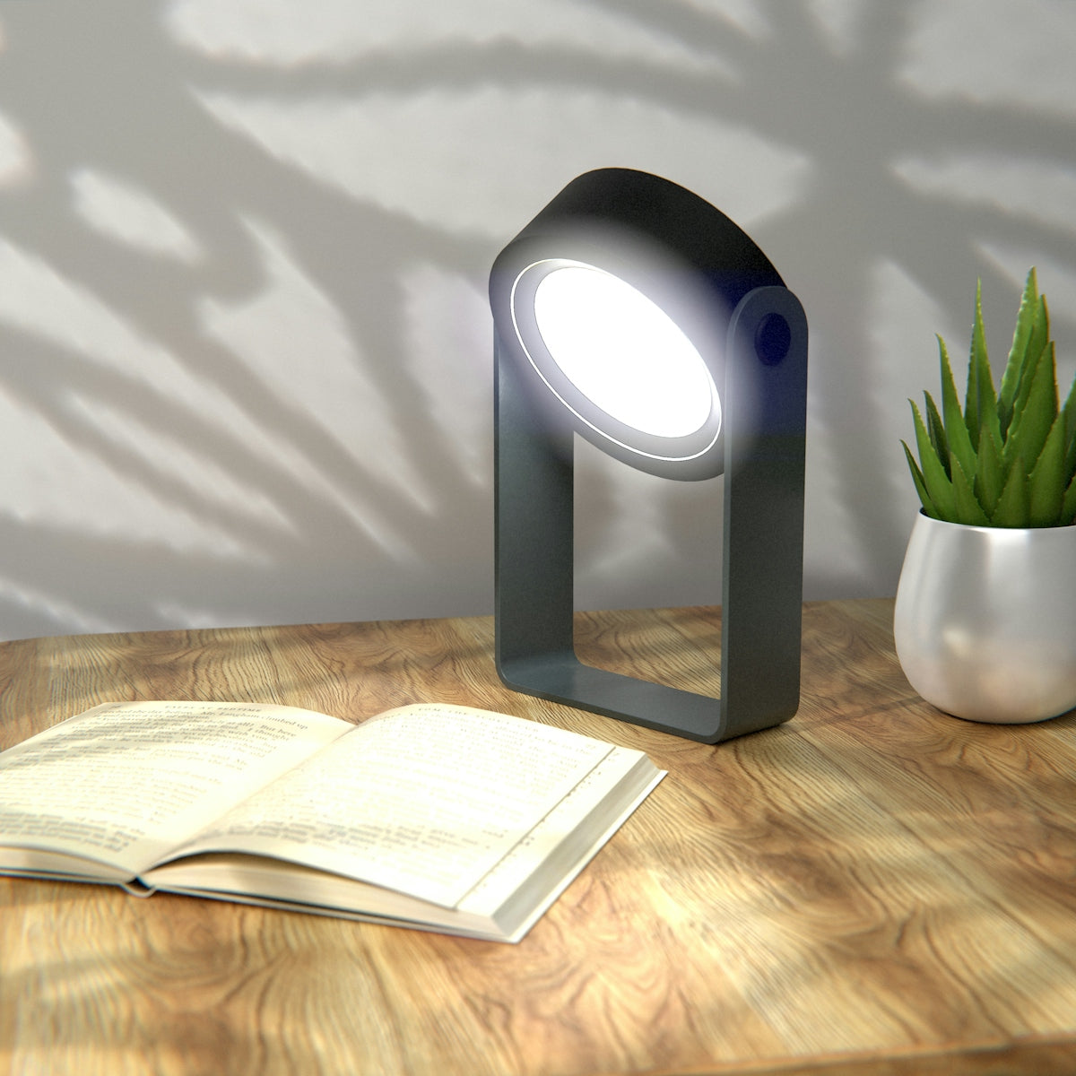 A portable lamp illuminates an open book on wooden desk