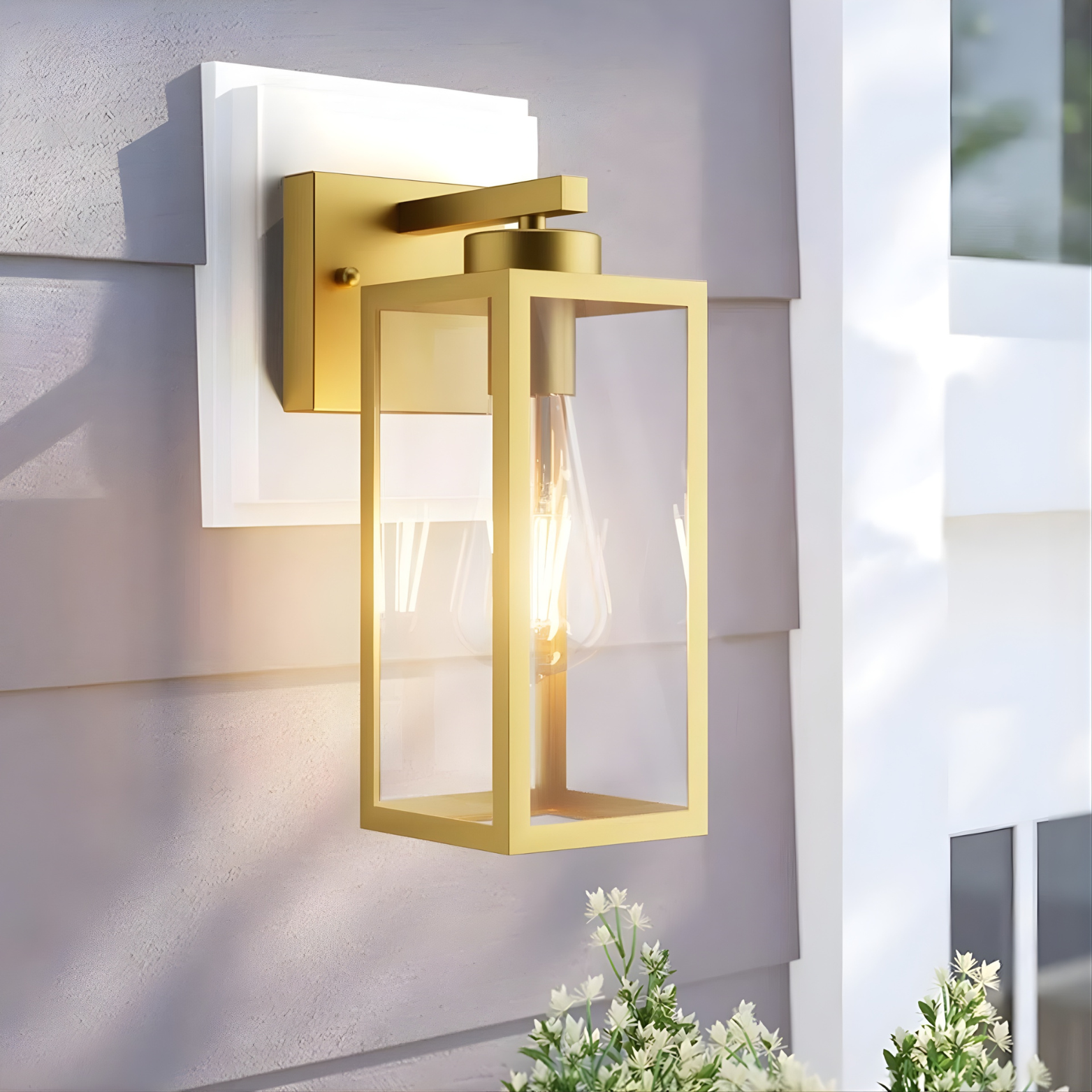 Gold outdoor wall light fixture on a building exterior with plants in the foreground.