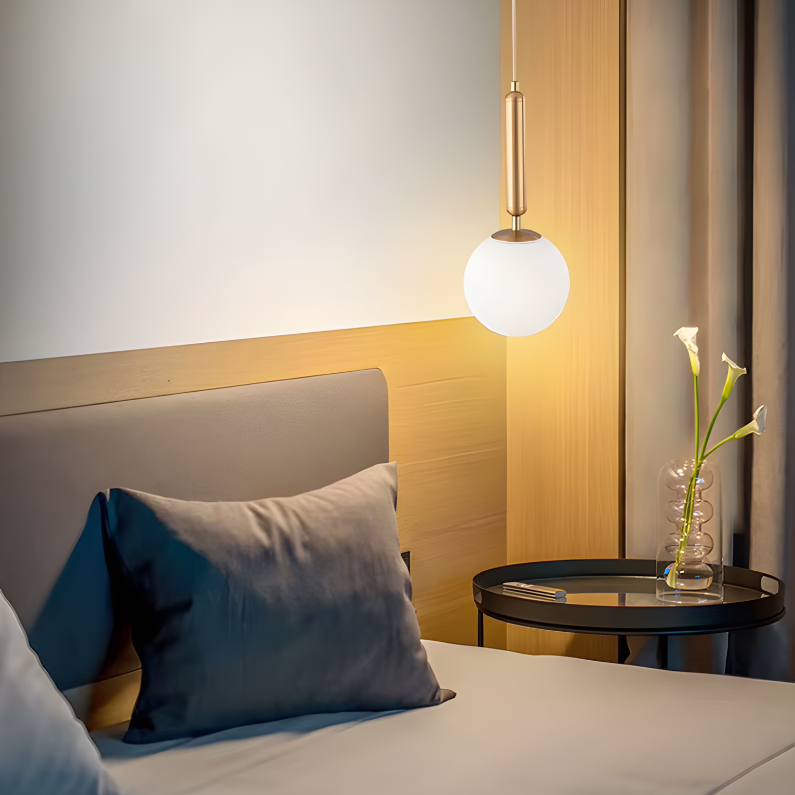 Neatly made bed with pillows and a small round table with a vase of flowers next to it.