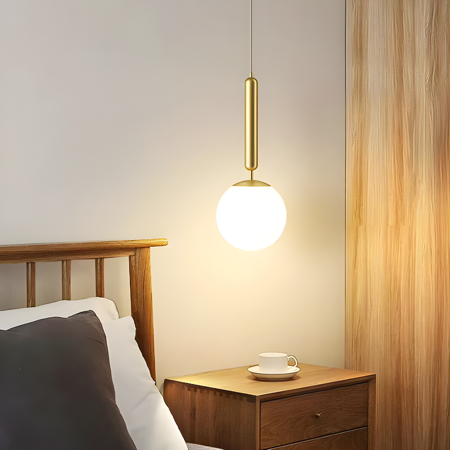 Gold pendant light above a wooden nightstand with a cup and saucer in a bedroom setting.