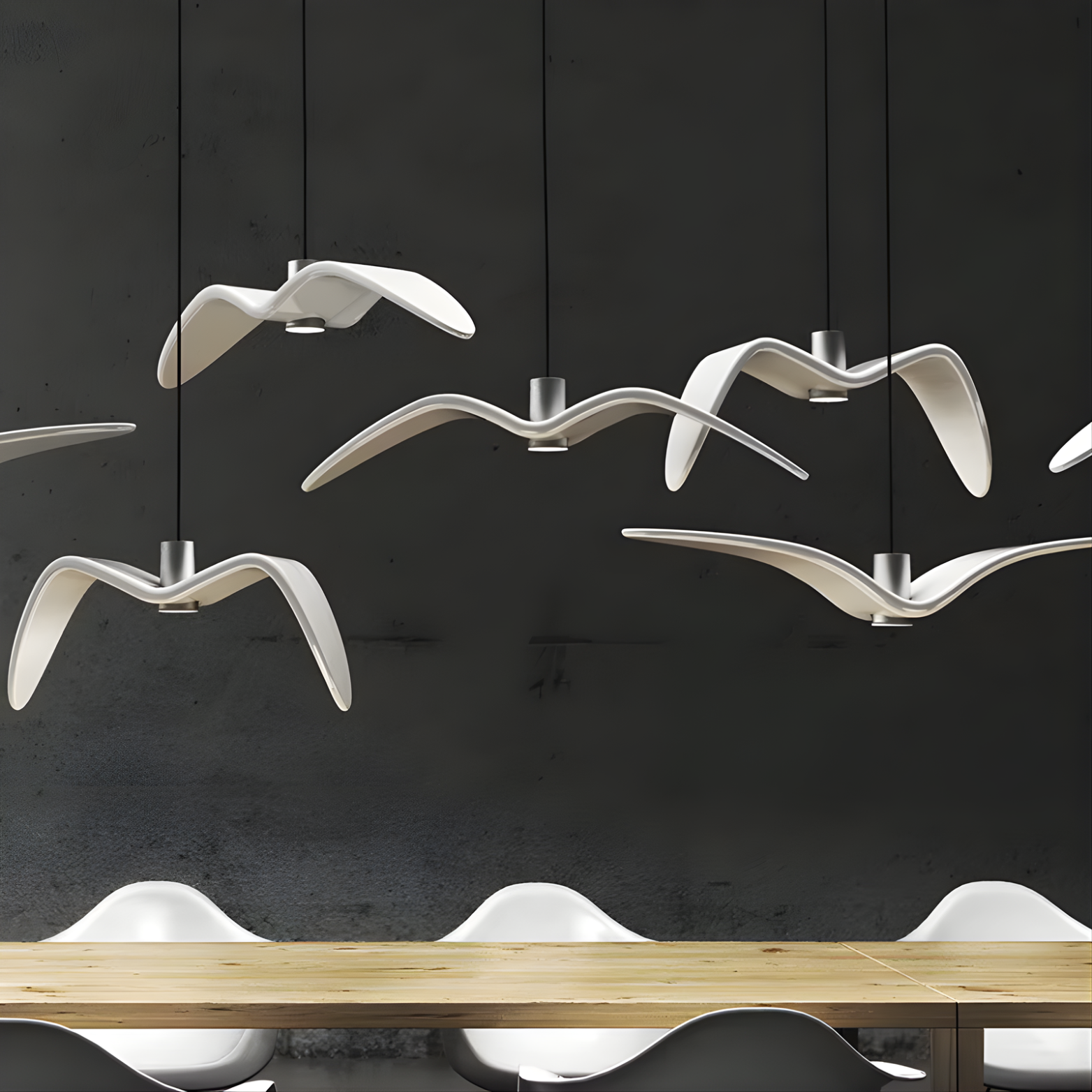 Modern chandelier designed like flying birds above a dining table with a dark wall background.