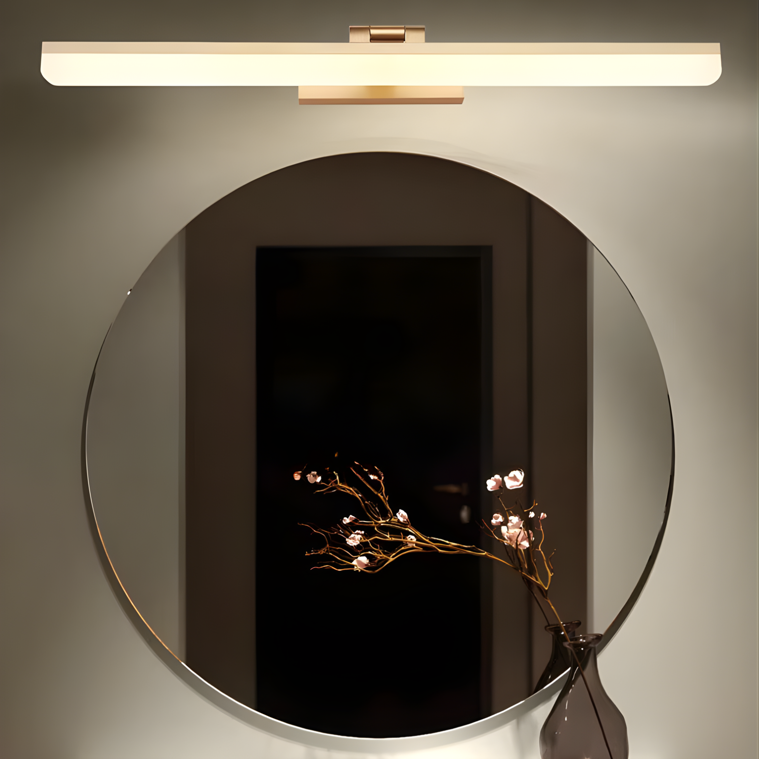 Round mirror with decorative branch and wall-mounted light fixture on a neutral background