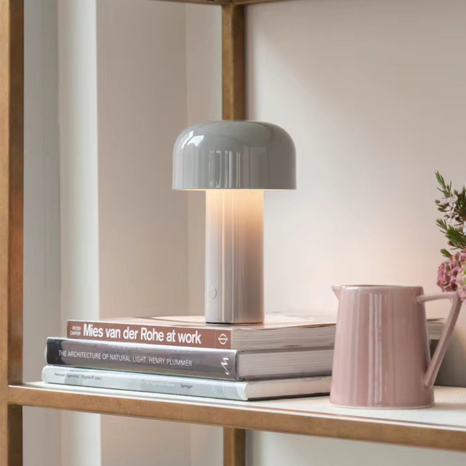 Gray table lamp on a stack of books with a pink pitcher and plant in the background